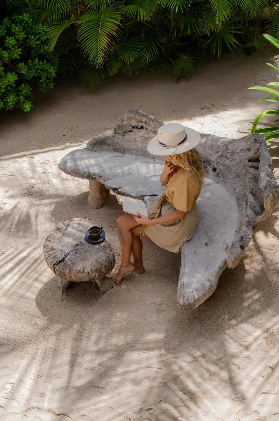 Woman reading on a carved wooden bench in the gardens at Encantada Tulum
