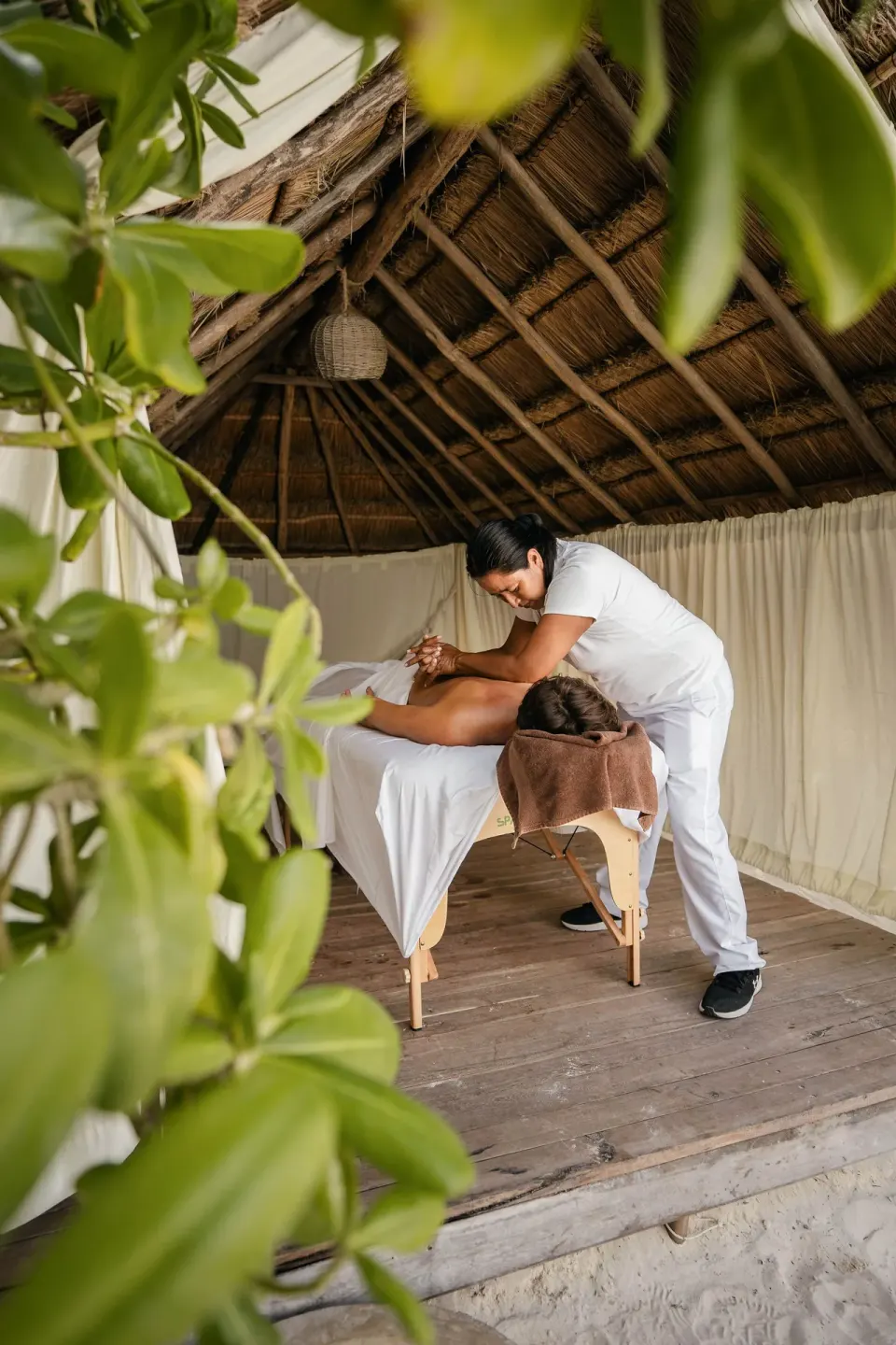 Massage therapist giving a table massage inside a thatched spa cabana at Encantada Tulum