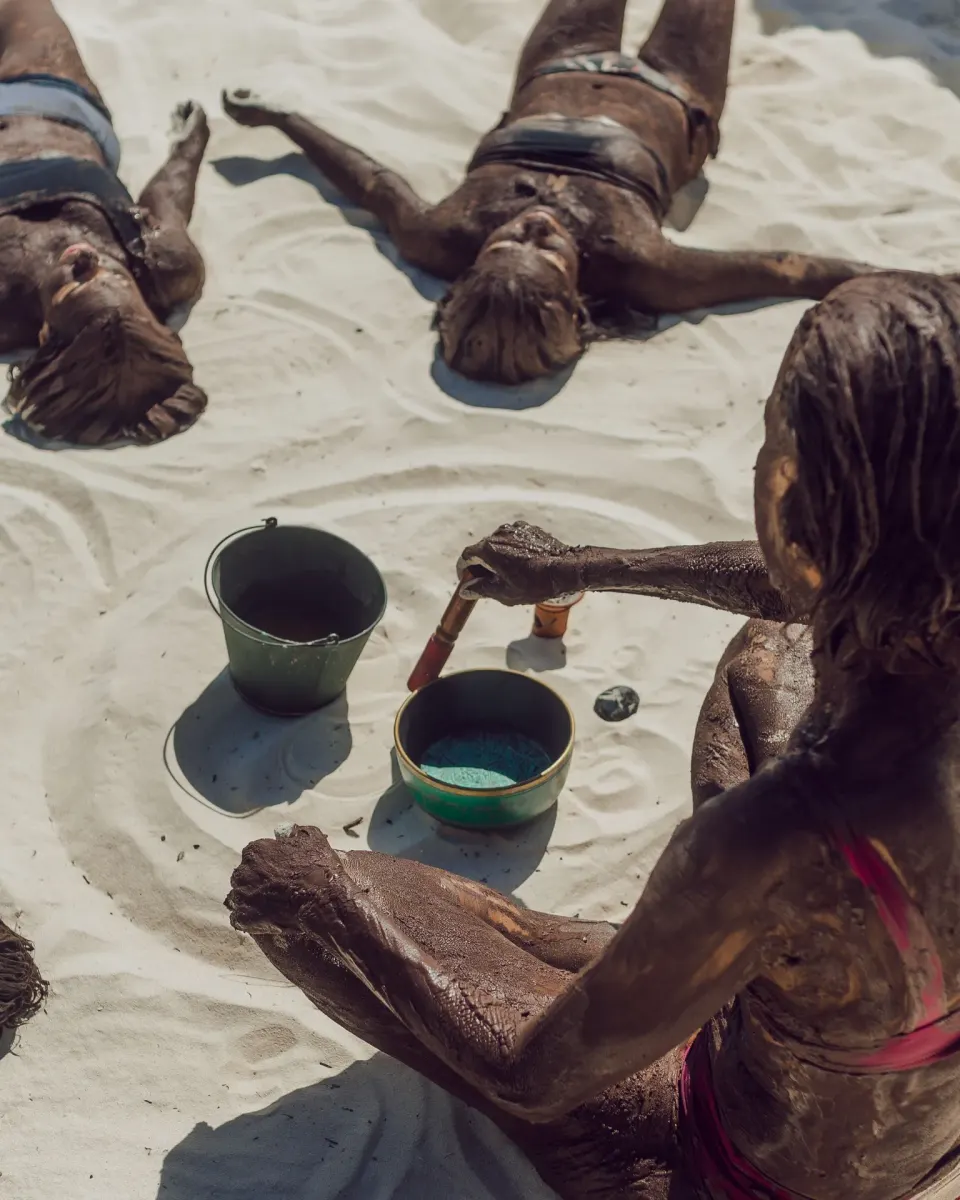 People covered in therapeutic mud on the sand during a spa mud treatment at Encantada Tulum