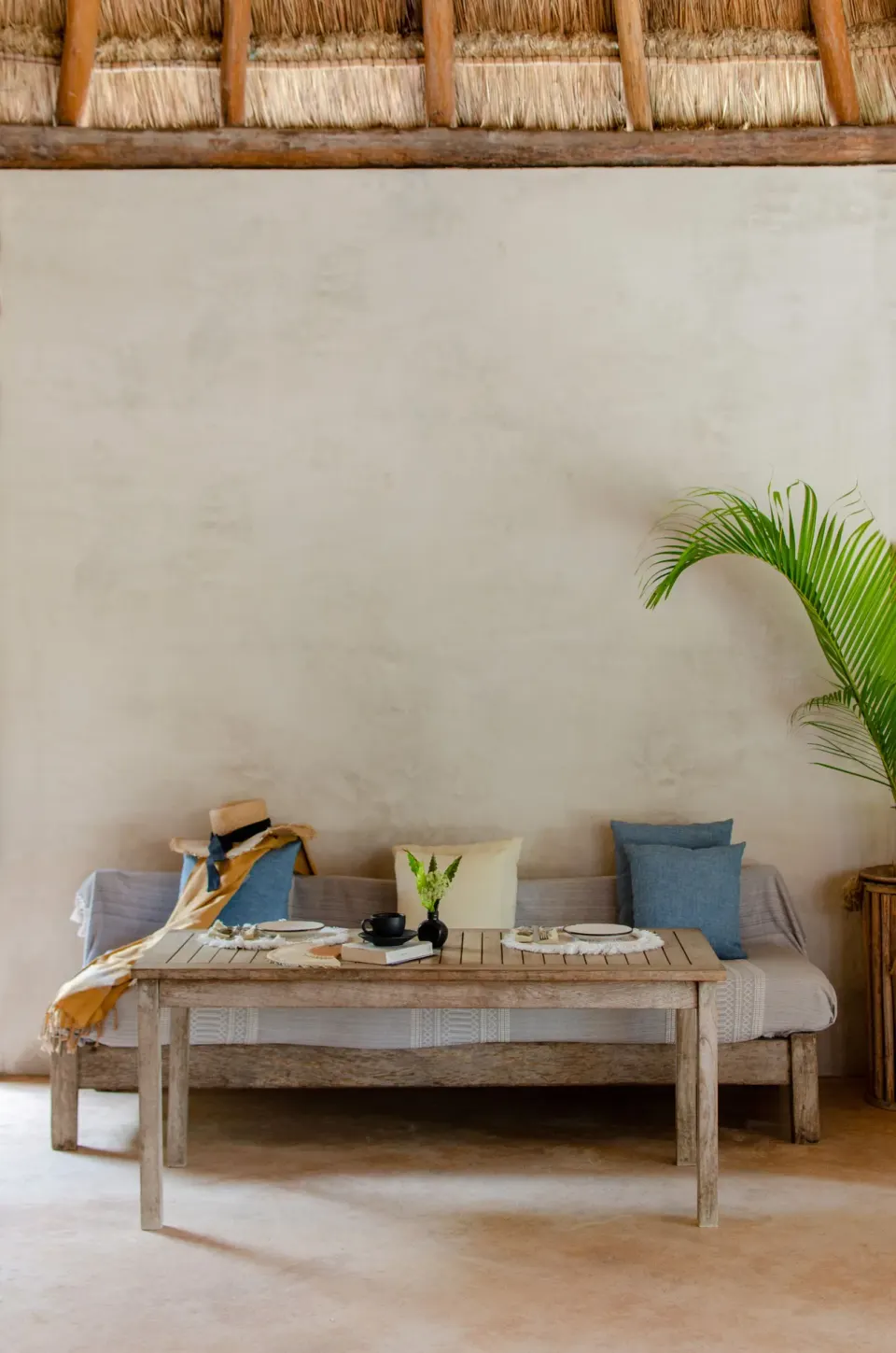 Low wooden table and cushioned bench seating under a palapa at Encantada Tulum.