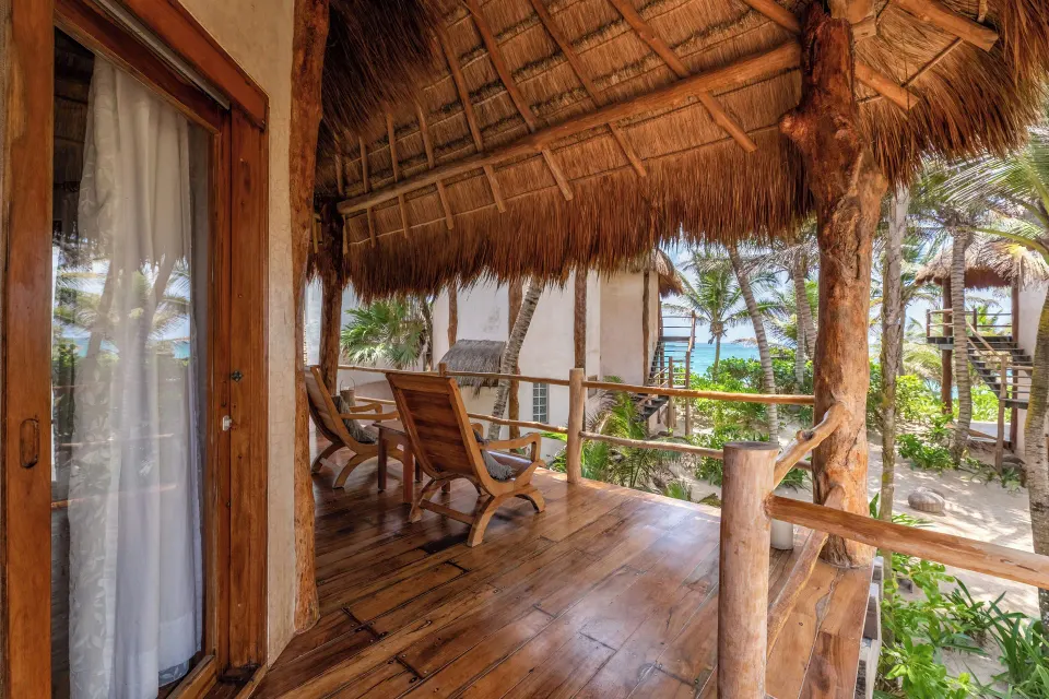 Thatched-roof private wooden terrace with lounge chairs and ocean glimpses at Encantada Tulum