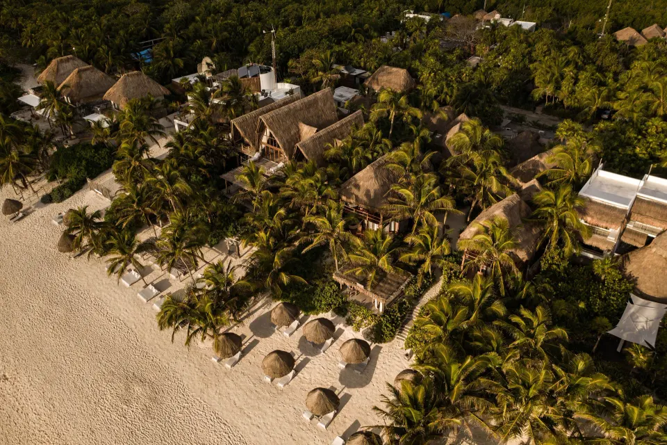 Aerial view of the Encantada Tulum resort along the beachfront with thatched roofs and palms