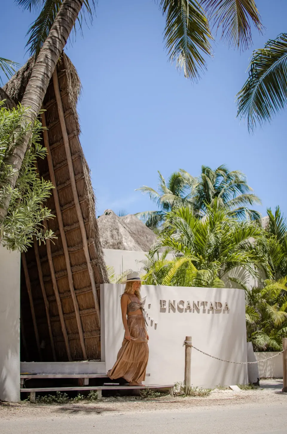 Woman posing by a curved entrance wall reading 'Encantada' at Encantada Tulum