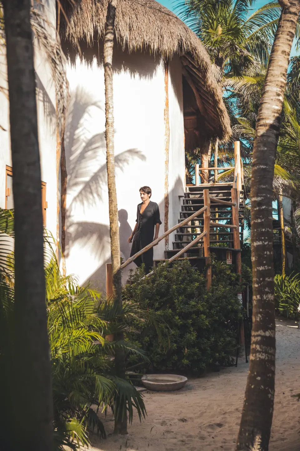 Guest descending wooden stairs by a white stucco bungalow at Encantada Tulum