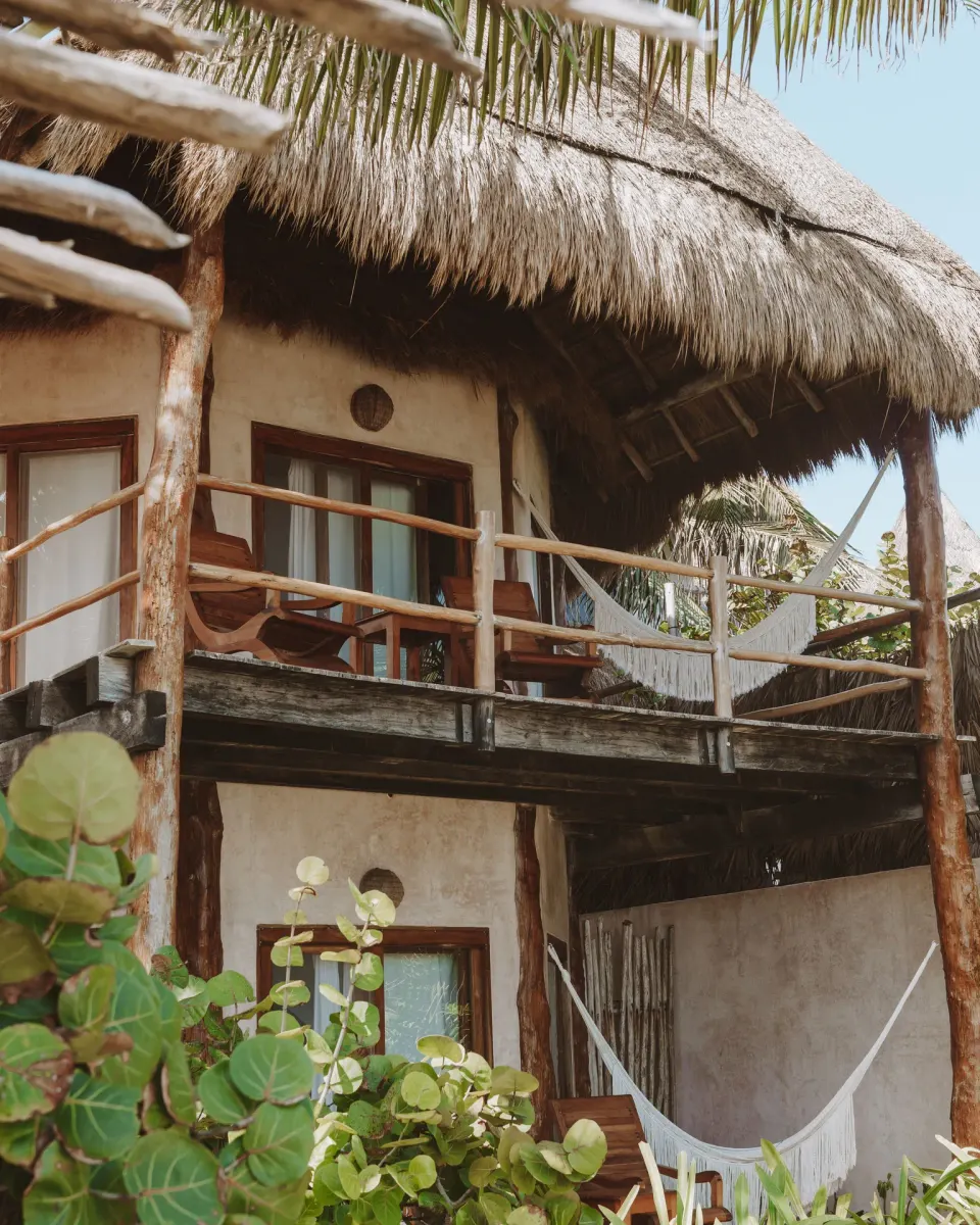Two-story thatched guest building with balcony and hammock at Encantada Tulum