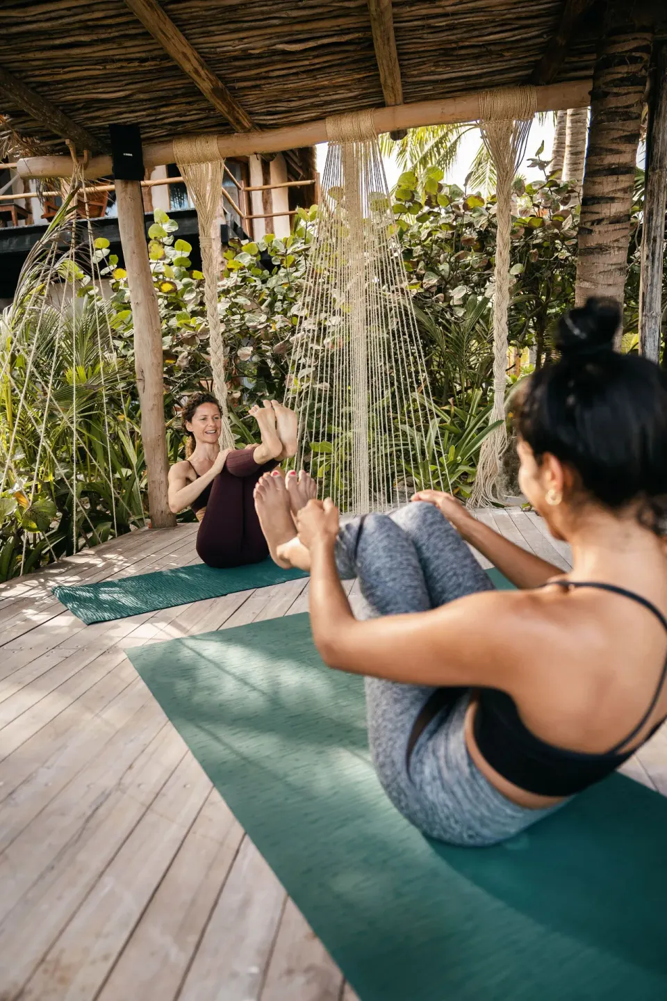 Two women doing partner yoga on mats under a thatched roof at Encantada Tulum