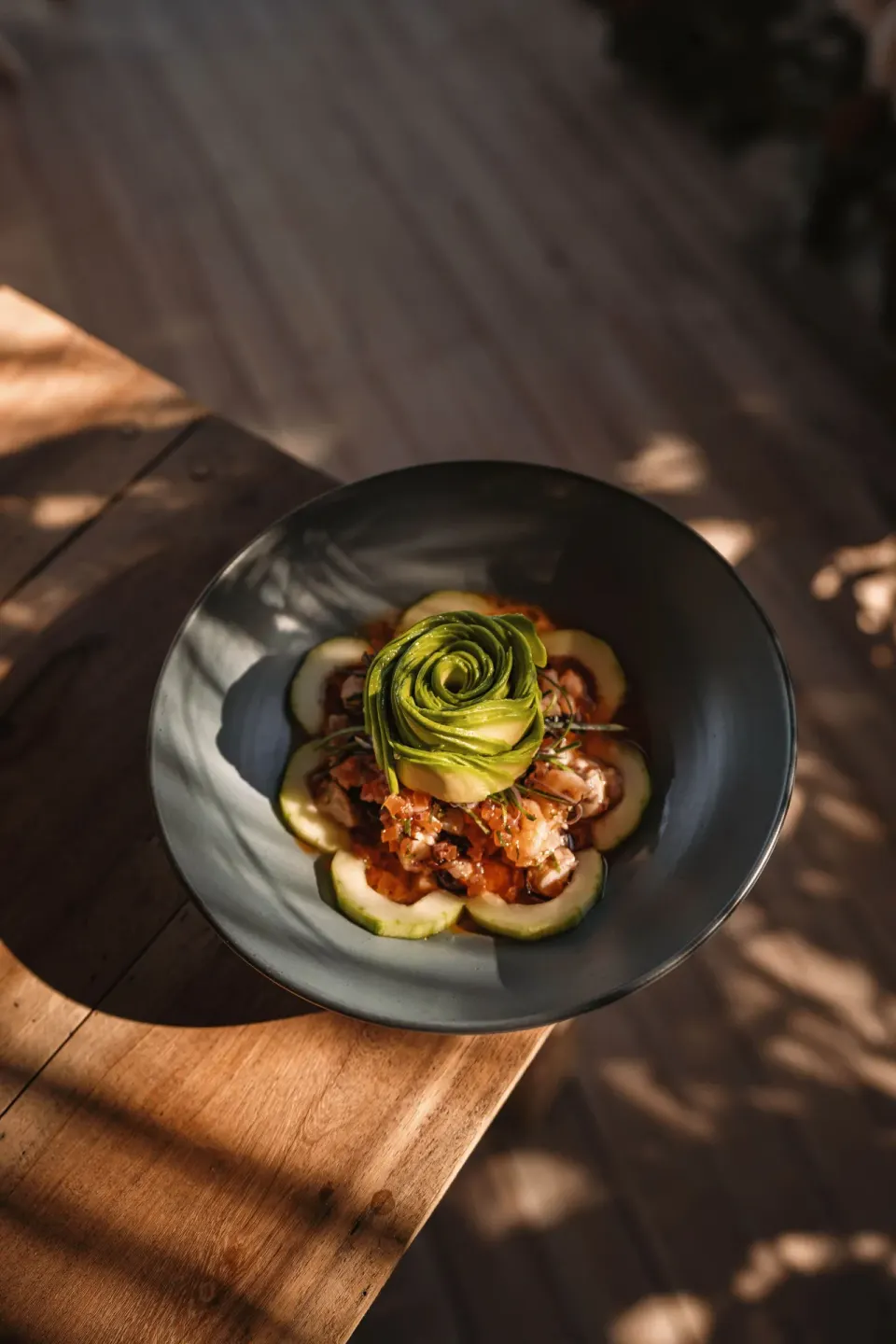 Bowl of food topped with a carved avocado rose on a wooden table at Encantada Tulum