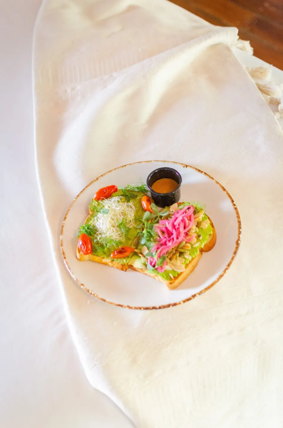 Avocado toast with pickled onions and dressing on a white plate at Encantada Tulum.