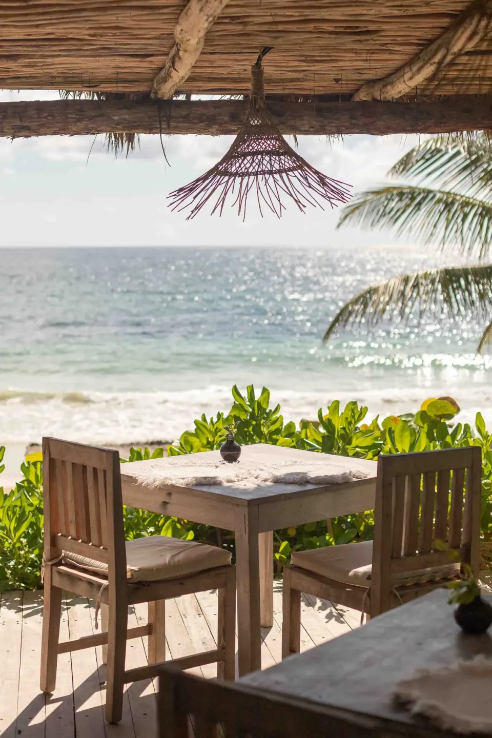 Wooden table and two chairs under a thatch palapa with ocean view at Encantada Tulum
