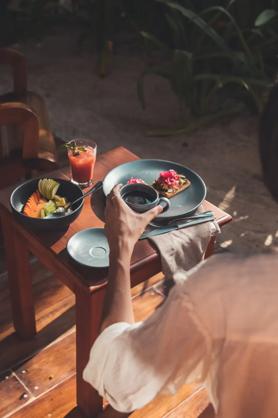 Guest reaching for a cup beside a plate of fruit and toast at Encantada Tulum