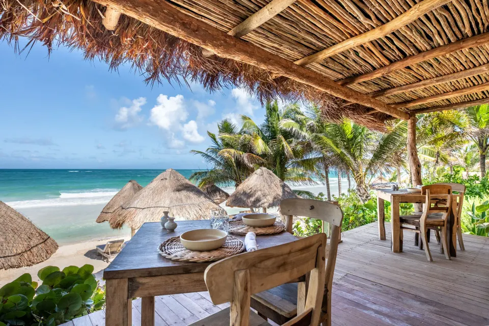 Thatched deck dining table overlooking the beach and palms at Encantada Tulum