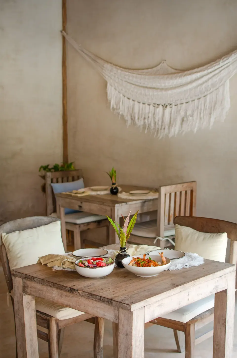 Wooden dining tables with woven placemats and a macramé wall hanging at Encantada Tulum.