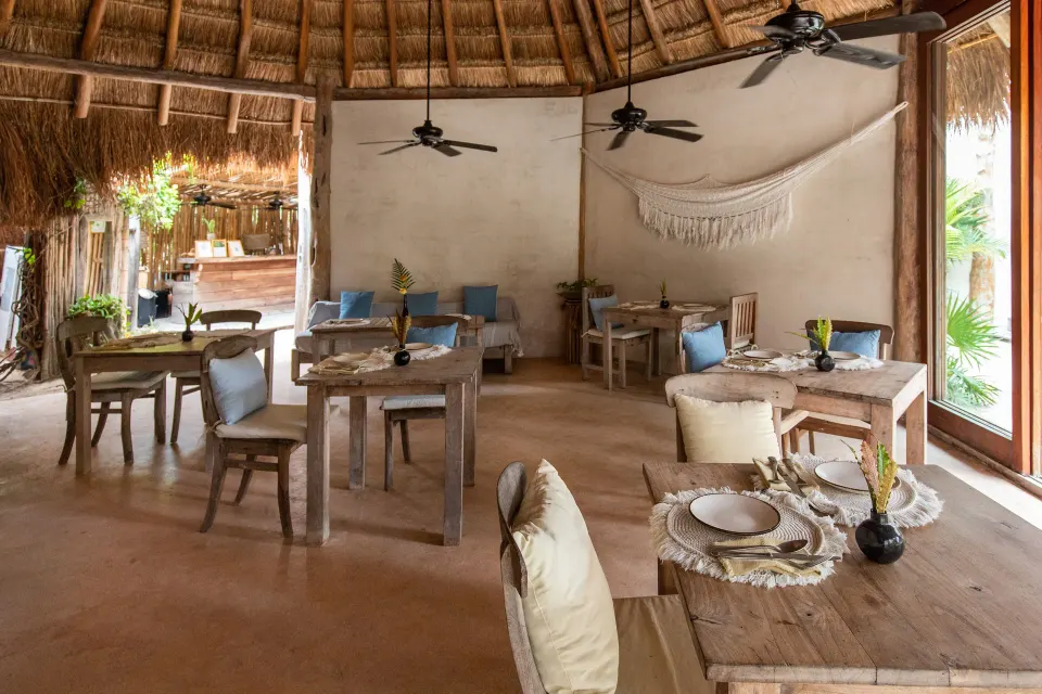 Open palapa dining room with wooden tables, chairs, and ceiling fans at Encantada Tulum.