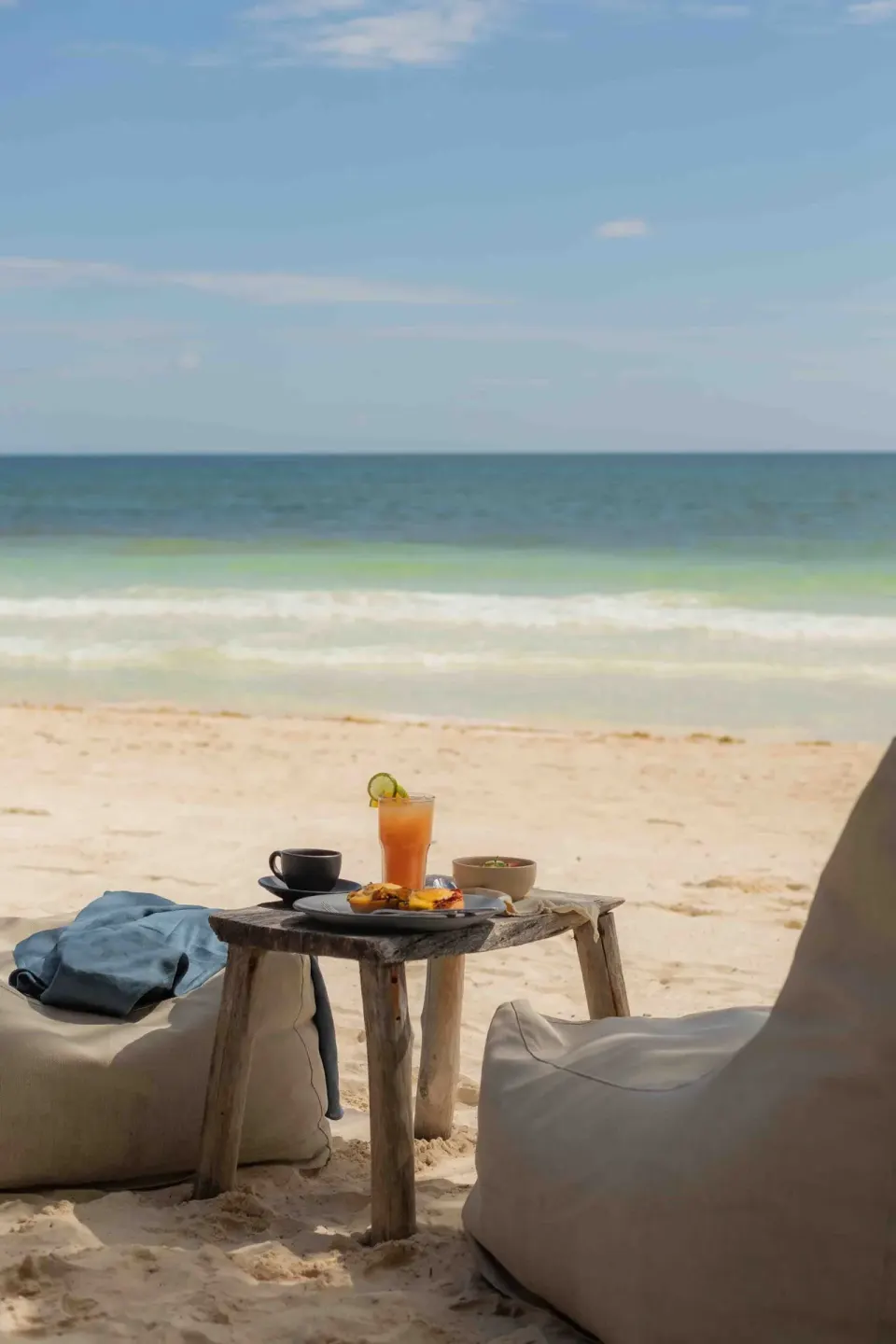 Low table with morning drink and breakfast between beanbags on the beach at Encantada Tulum