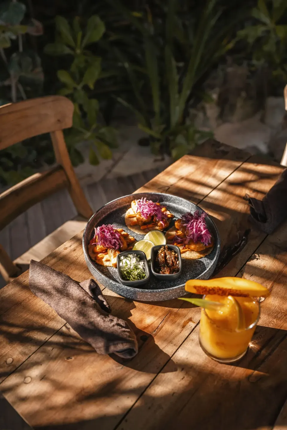 Plate of three tostadas with two small salsas and a tropical drink on a wooden table at Encantada Tulum
