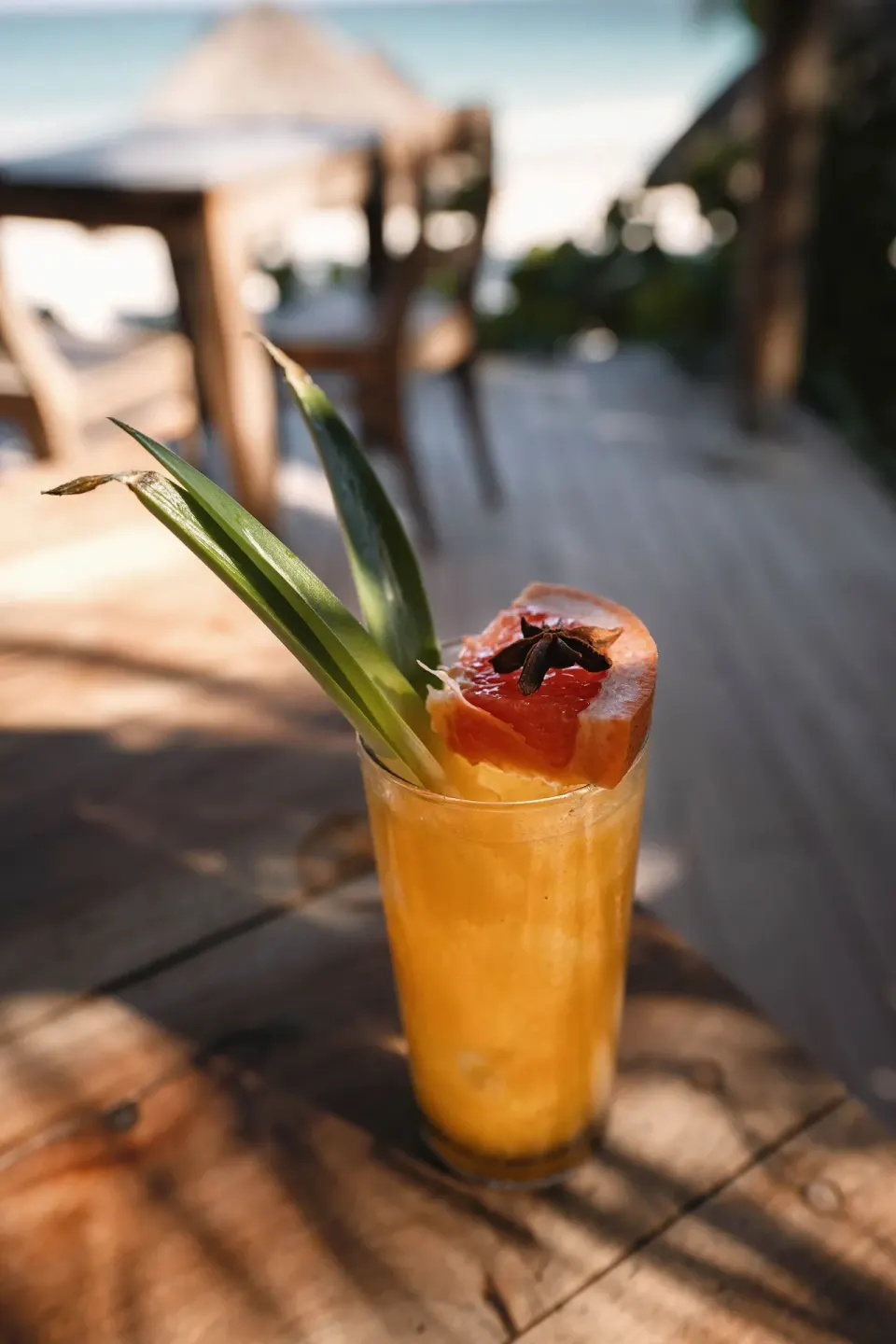Tall tropical cocktail garnished with papaya and pineapple leaf on a wooden table at Encantada Tulum