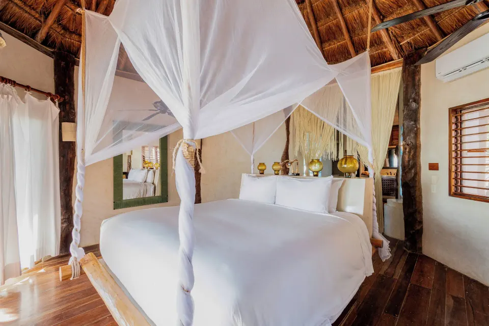 Bright four-poster king bed and natural wood interior in the Beach Front Upper Room at Encantada Tulum