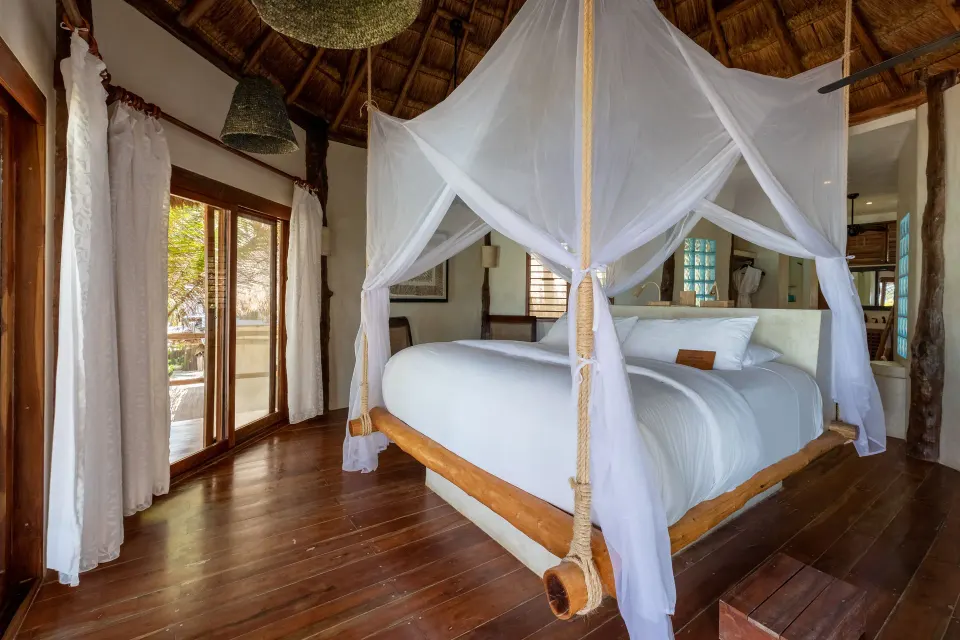 Four-poster king bed and open bathroom passage in the Beach Front Upper Room at Encantada Tulum