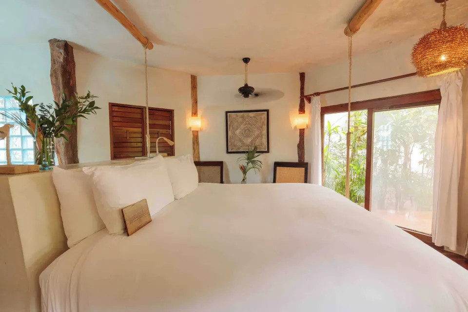 Close-up view of a large white king bed and bedside pendant lights in a Garden View Room at Encantada Tulum.