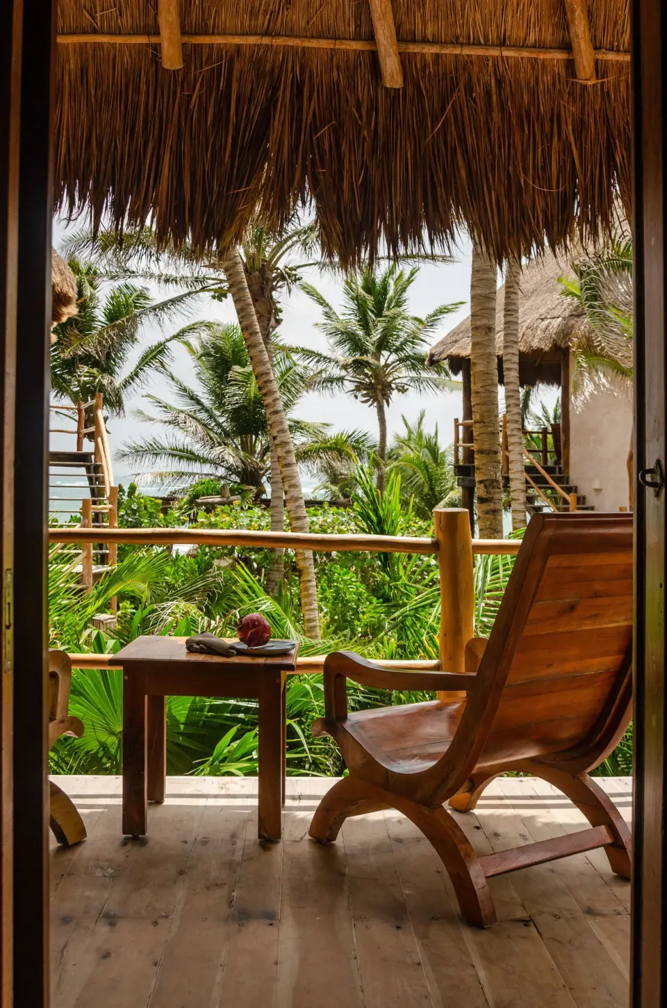 Balcony view from Partial Ocean View Room showing wooden chair, table and palms at Encantada Tulum