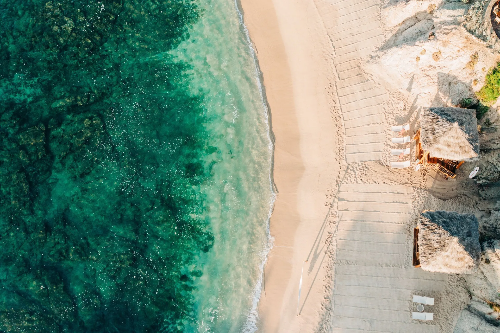 Aerial view of turquoise water, sandy beach, and thatched umbrellas at Esperanza.