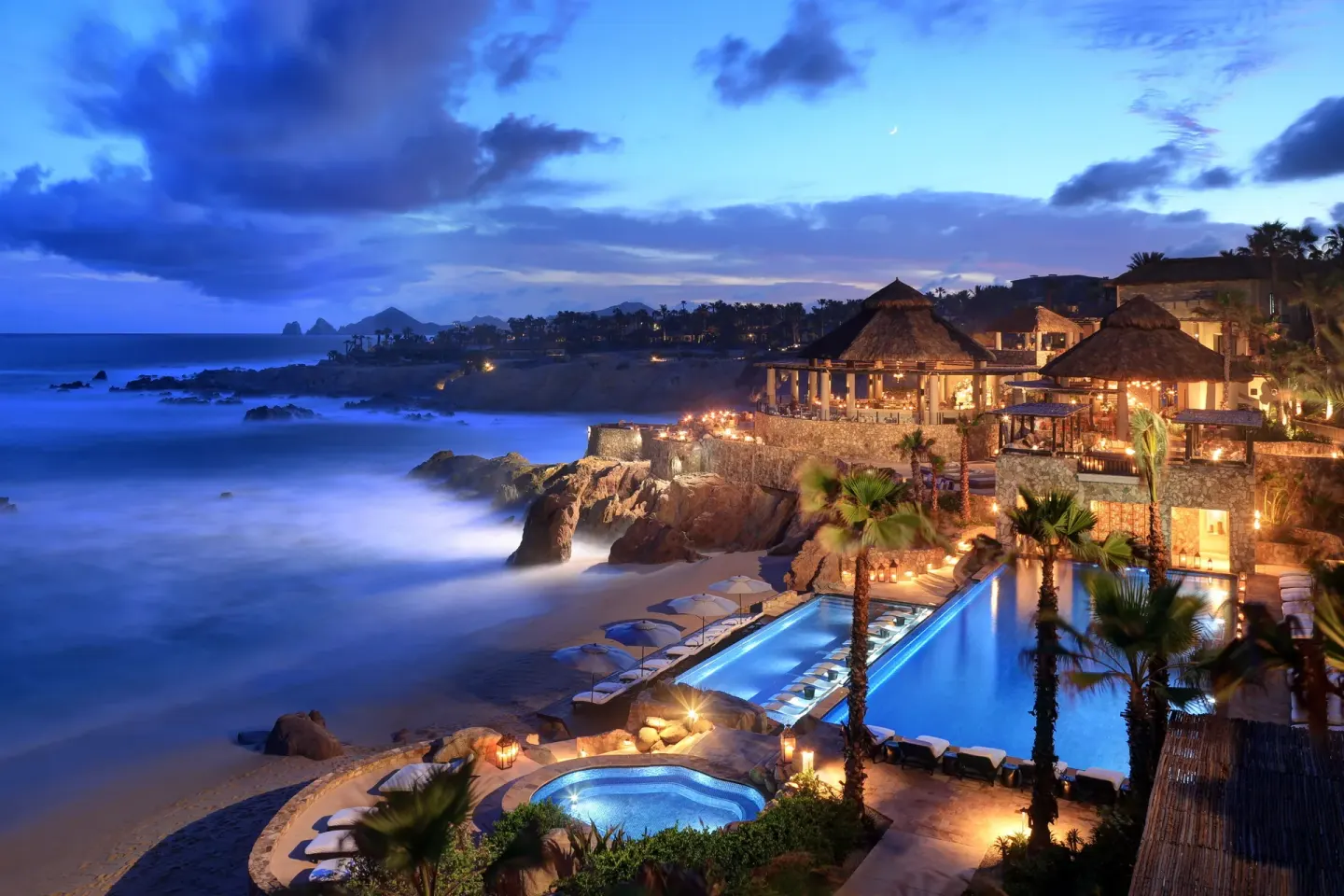 Blue-hour view of illuminated pools, beach, and oceanfront buildings at Esperanza.
