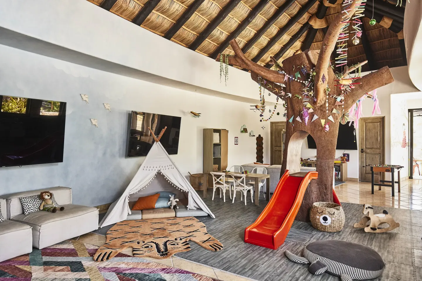Children’s playroom with a teepee, slide, toys, and thatched ceiling at Esperanza.