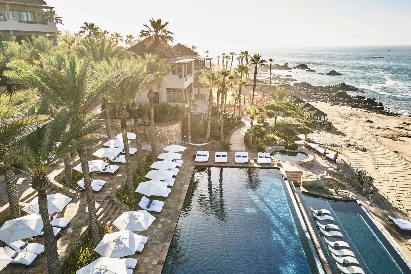 Oceanfront pool deck with white umbrellas and beach below at Esperanza.