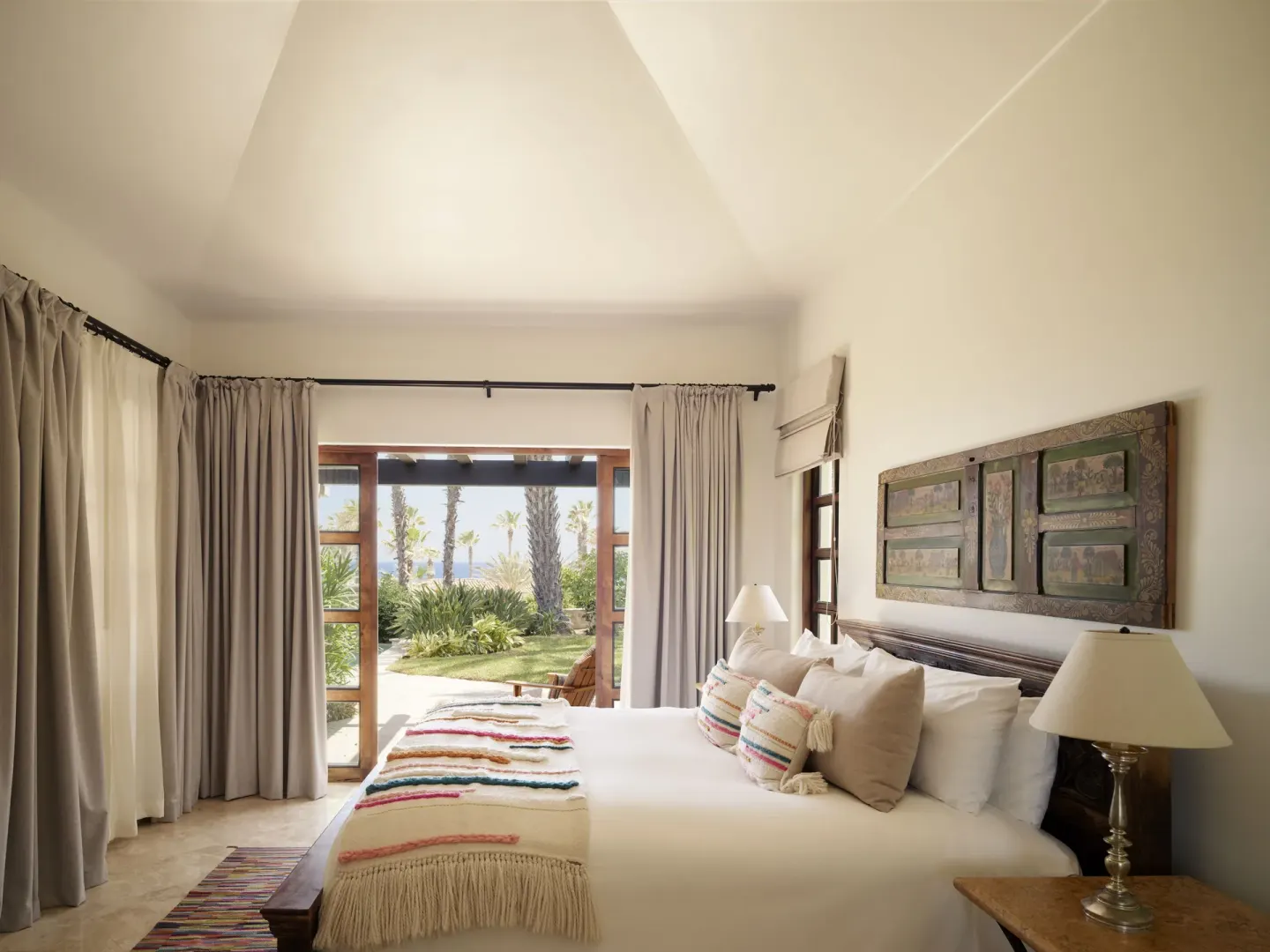 Guest room with king bed, colorful textiles, and open doors to palms at Esperanza.