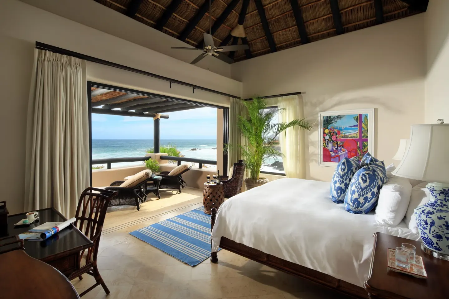 Villa bedroom with king bed, thatched ceiling, and terrace loungers at Esperanza.
