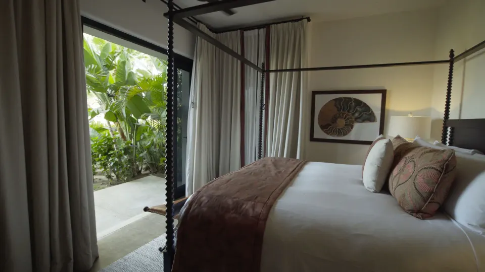 Villa bedroom with a dark four-poster bed beside a garden patio at Esperanza.