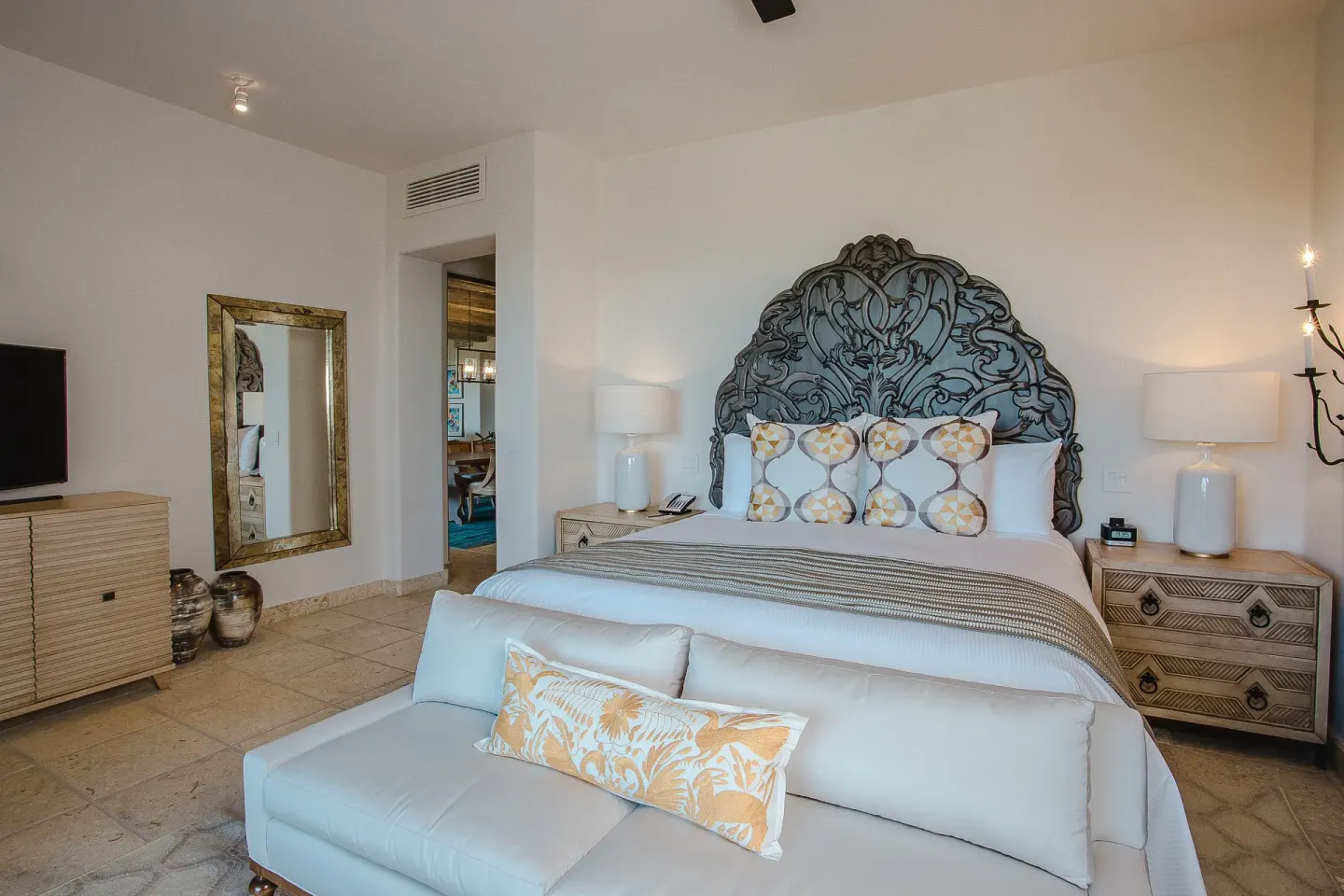Villa bedroom with a king bed, carved headboard, sofa, and TV at Esperanza.