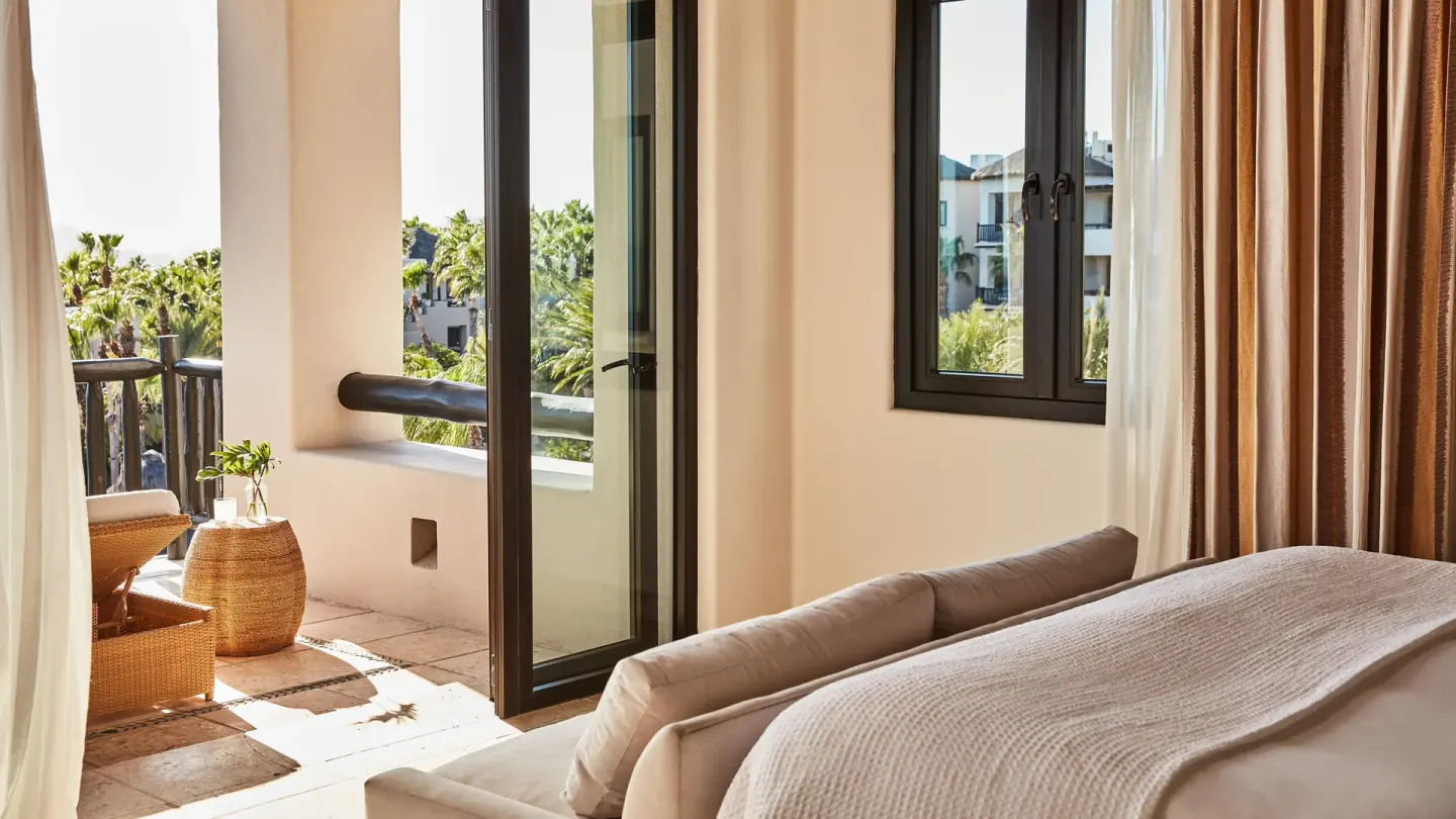 A villa bedroom at Esperanza opens onto a balcony with wicker seating and palm views.