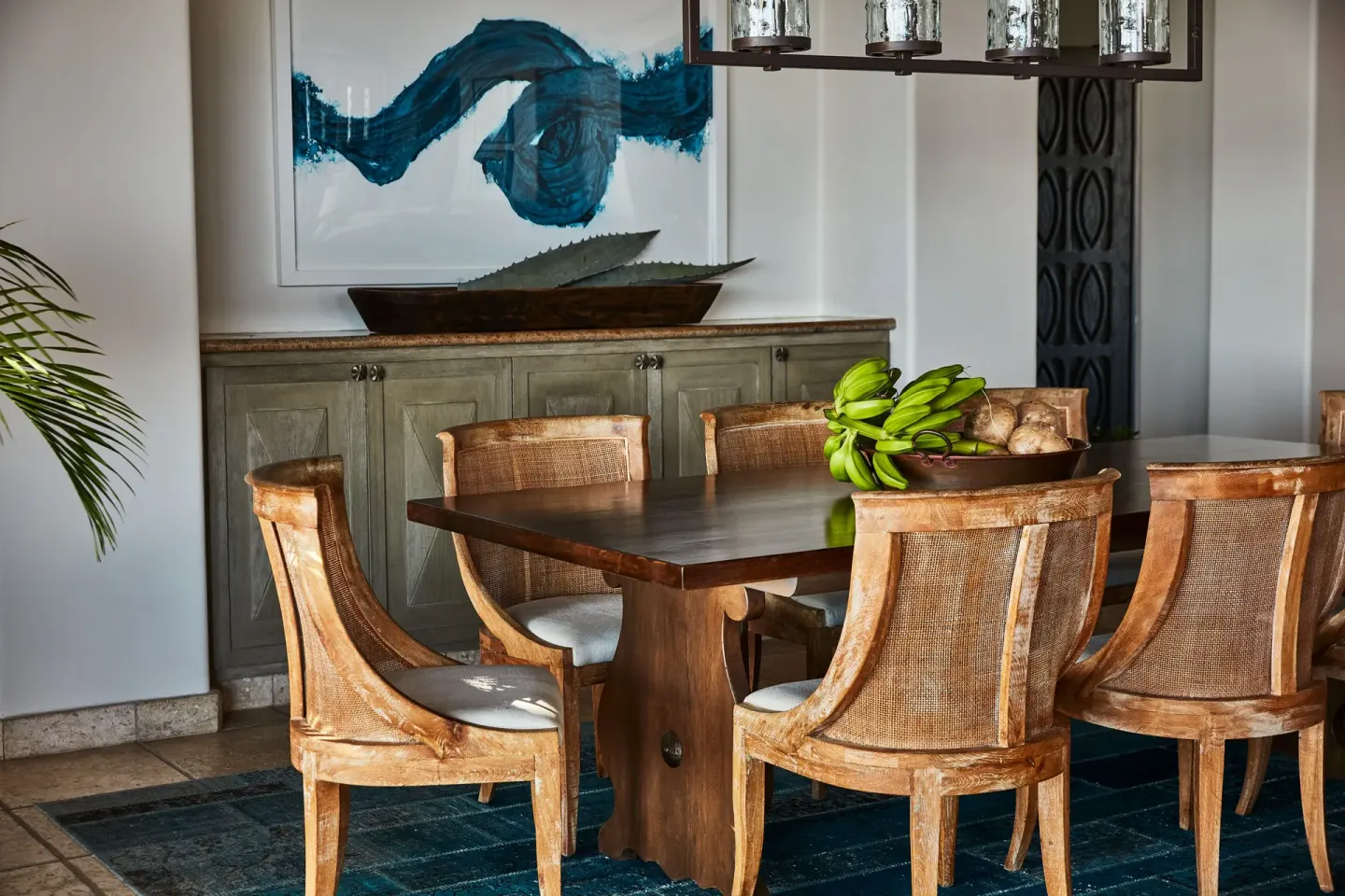 A villa dining area at Esperanza shows a wood table, cane chairs, fruit bowl, and blue artwork.