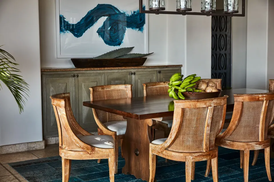 A villa dining area at Esperanza shows a wood table, cane chairs, fruit bowl, and blue artwork.