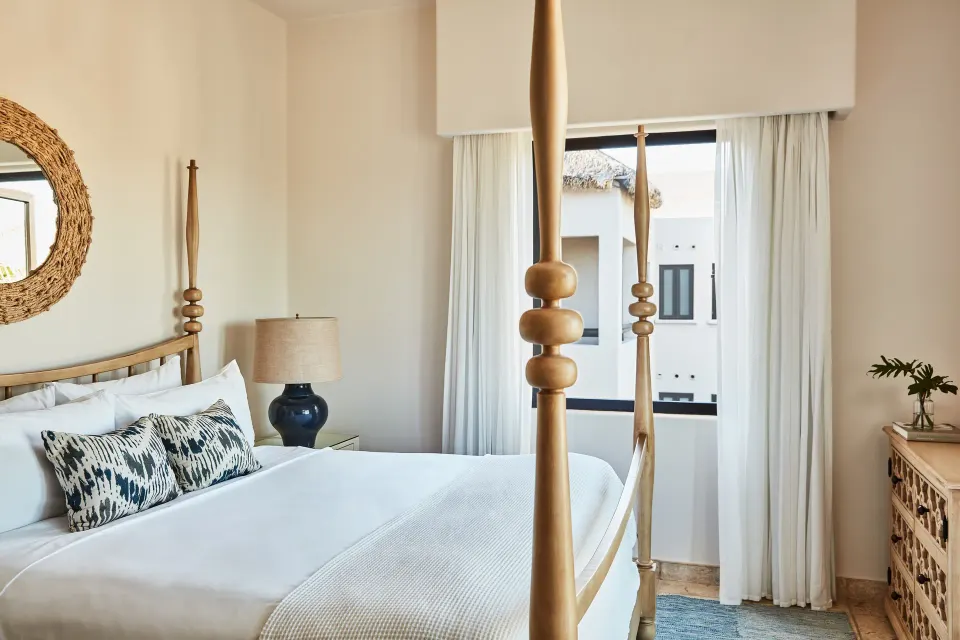 A wood four-poster bed in a villa bedroom at Esperanza beside a window and carved dresser.