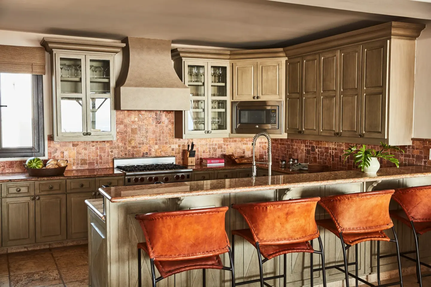 A villa kitchen at Esperanza has a long island, bar stools, wood cabinets, and tile backsplash.