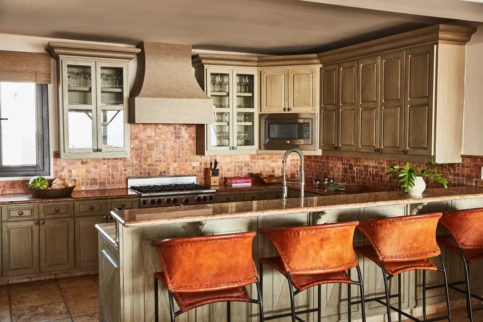 A villa kitchen at Esperanza has a long island, bar stools, wood cabinets, and tile backsplash.