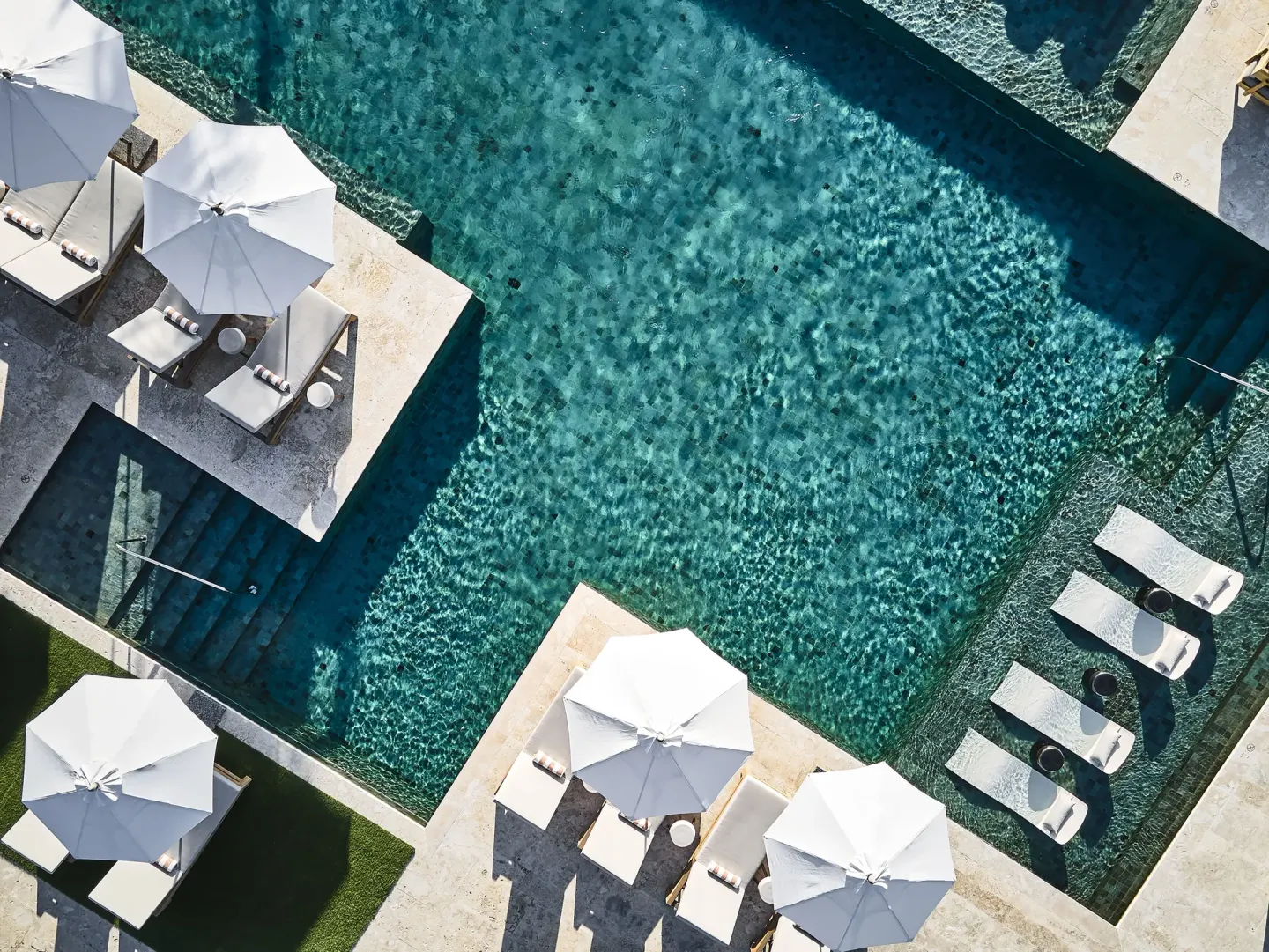 Aerial view of a turquoise resort pool with white umbrellas at Etéreo, Auberge Collection.