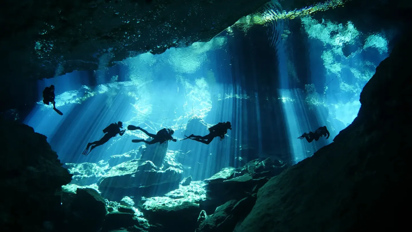 Scuba divers swim through a blue cenote cave near Etéreo, Auberge Collection.
