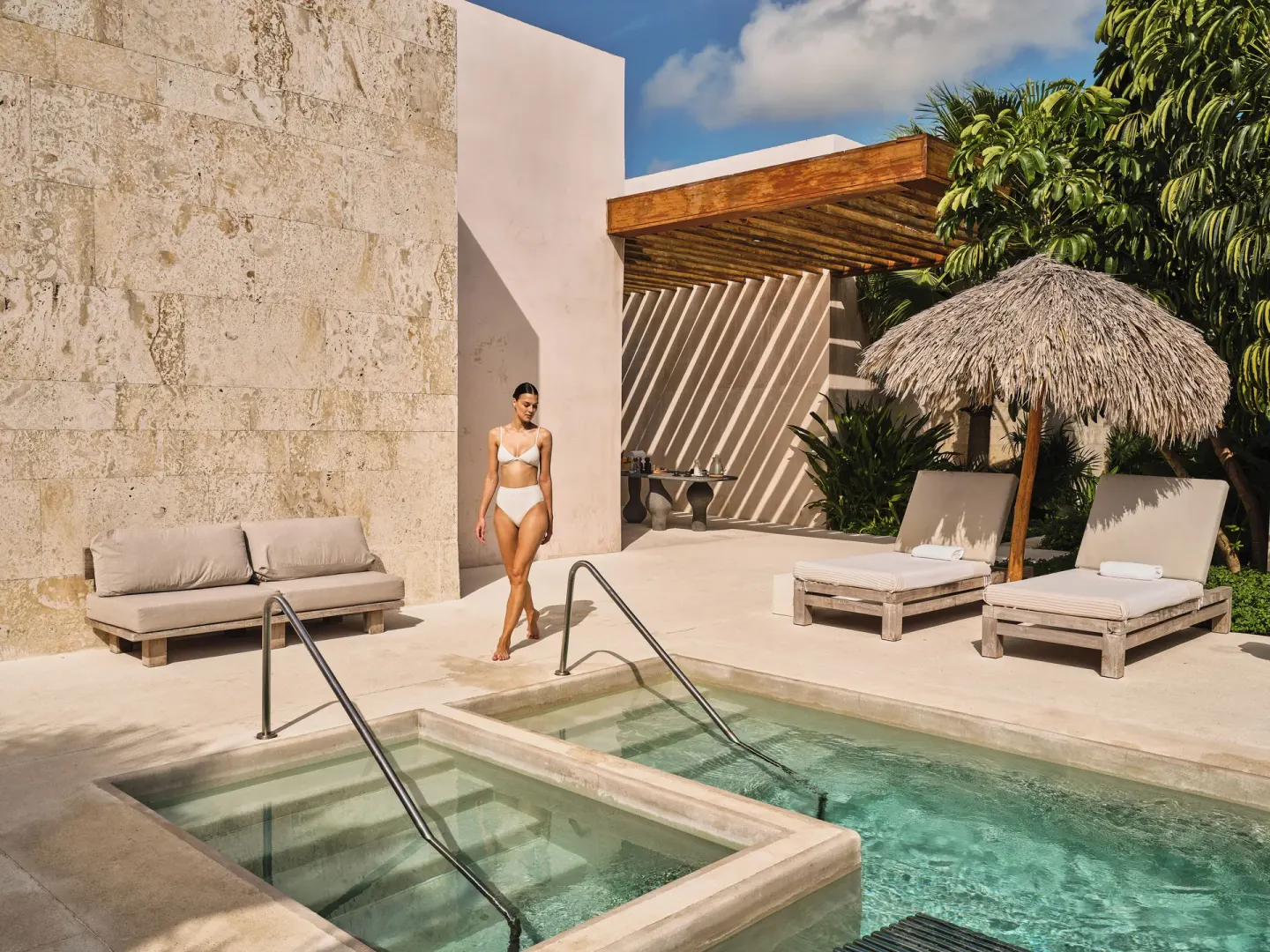 Spa pool with loungers, thatched umbrella, and stone walls at Etéreo, Auberge Collection.
