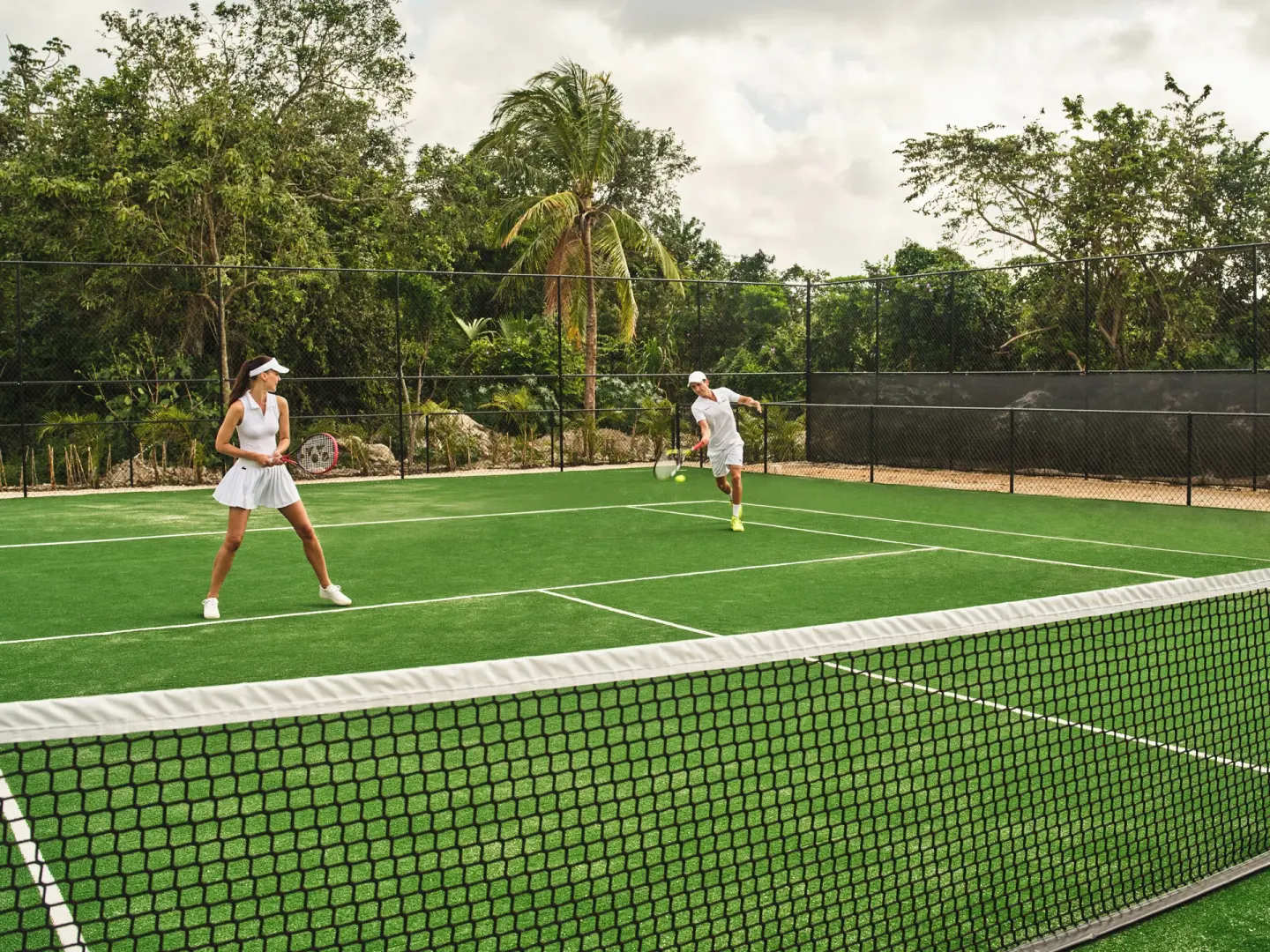Two tennis players on a green court at Etéreo, Auberge Collection.