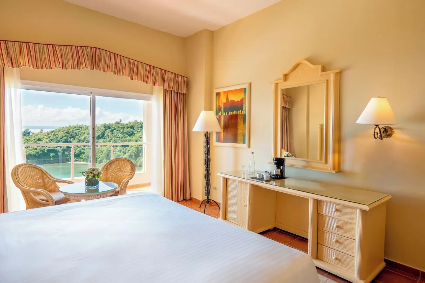 Deluxe Room Sea View bed, desk, and green hillside outlook at Eurostars Grand Cayacoa.