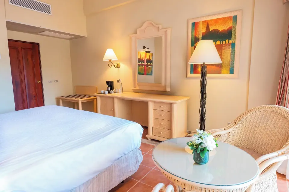 Deluxe Room with king bed, vanity, mirror, and wicker chairs at Eurostars Grand Cayacoa.