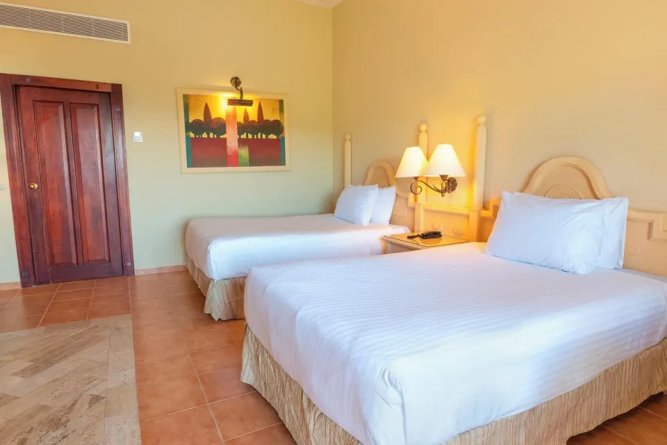 Deluxe Room with two beds, entry door, wall art, and bedside lamps at Eurostars Grand Cayacoa.