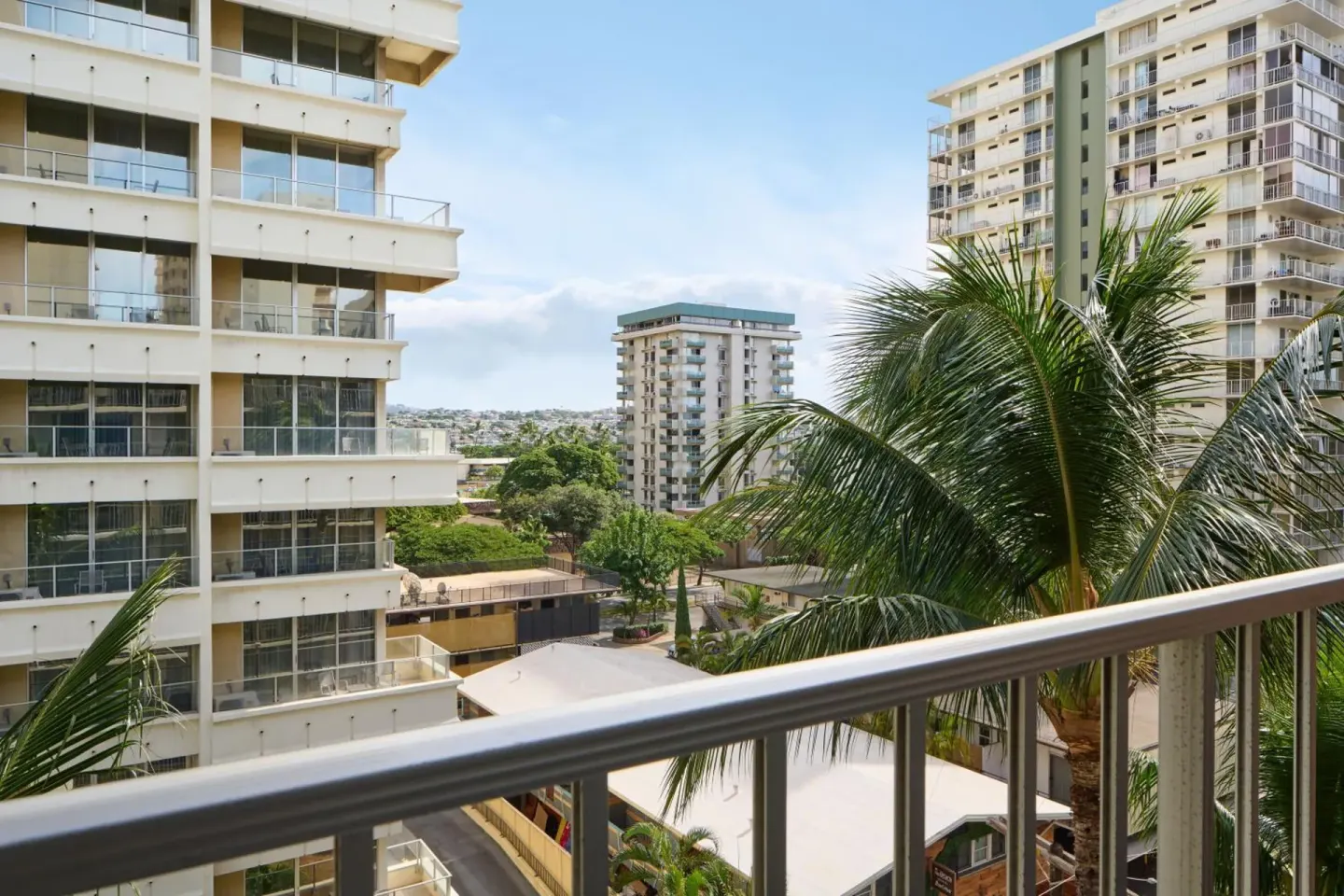 Balcony railing with palm trees and nearby high-rises at Ewa Hotel Waikiki.