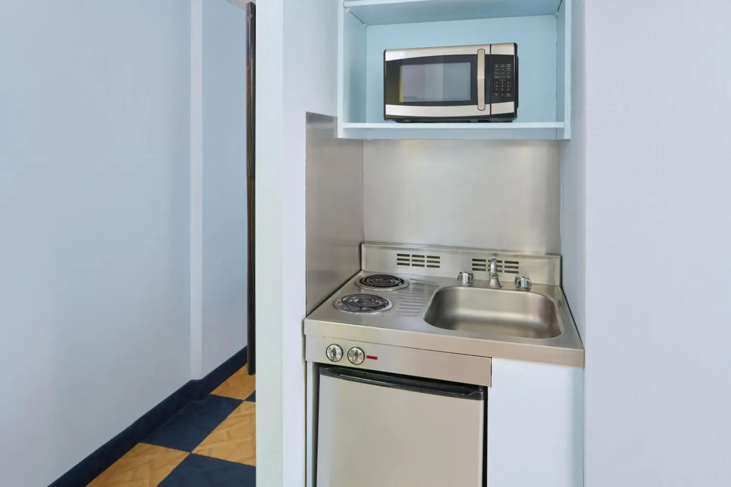 Compact kitchenette with cooktop, sink and microwave at Ewa Hotel Waikiki.