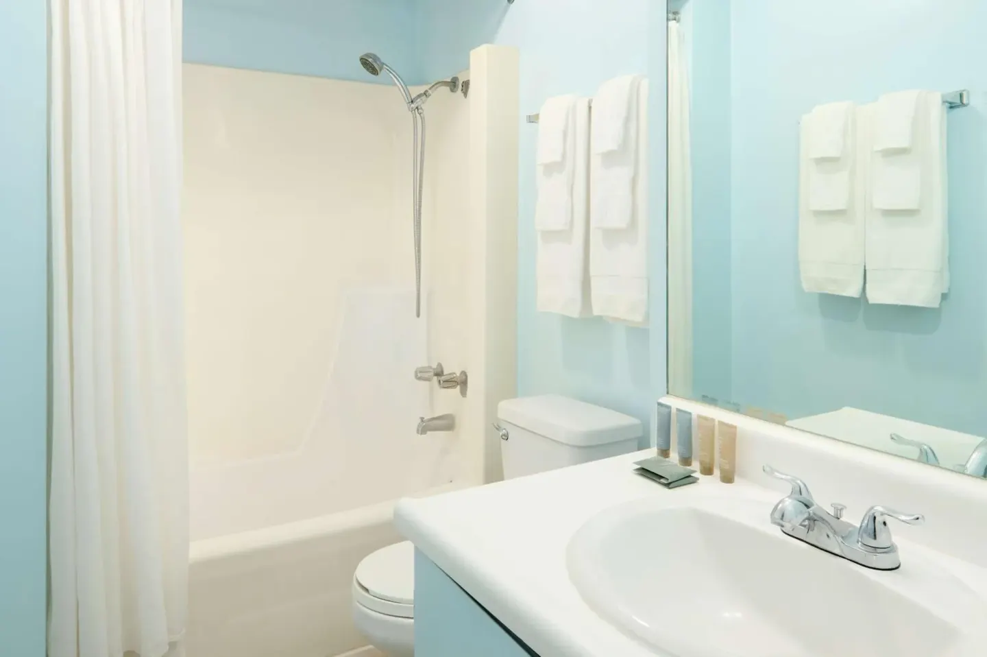 Guest bathroom with blue walls, vanity and tub-shower at Ewa Hotel Waikiki.