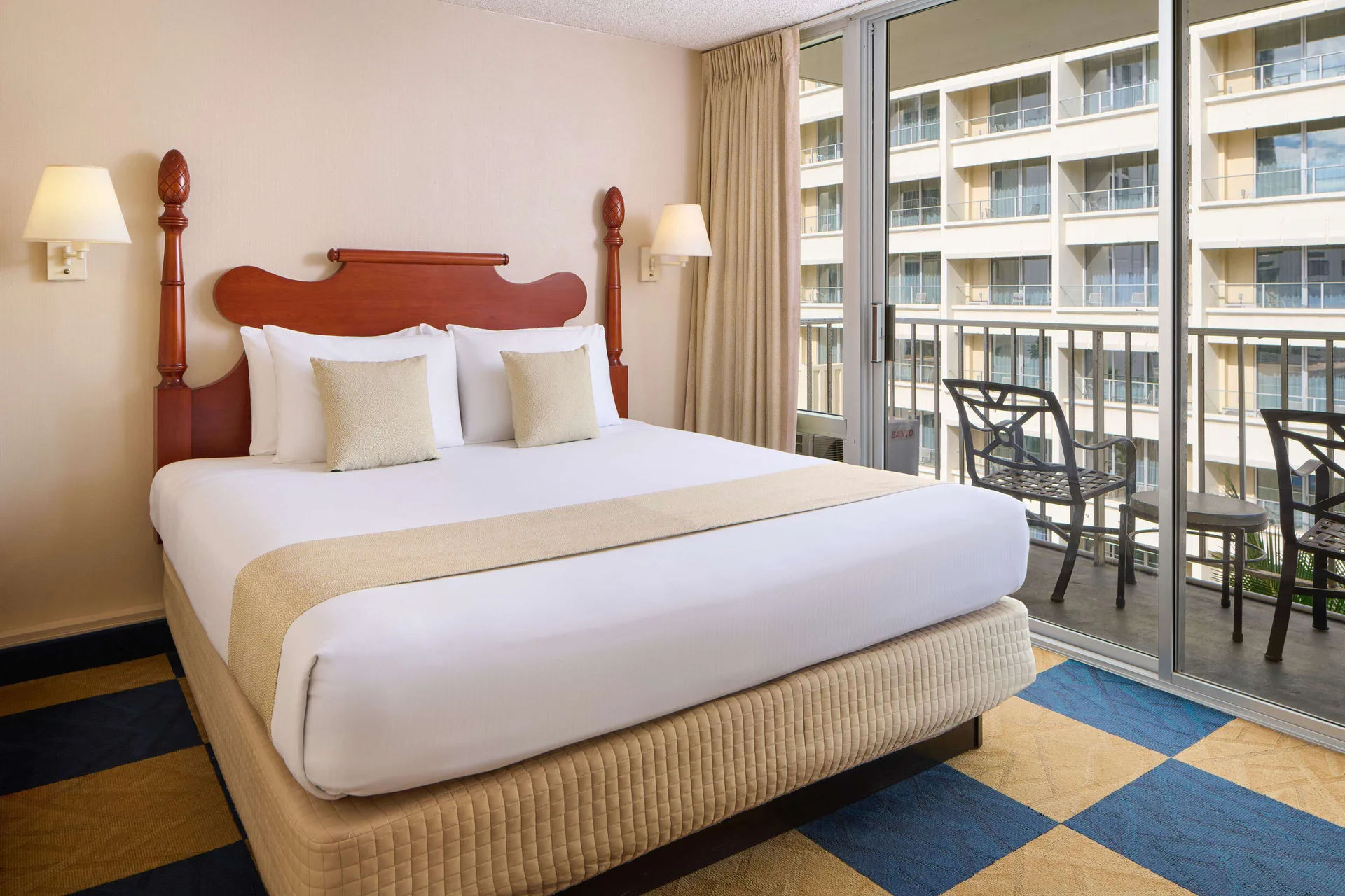 Guest room with king bed and balcony seating at Ewa Hotel Waikiki.