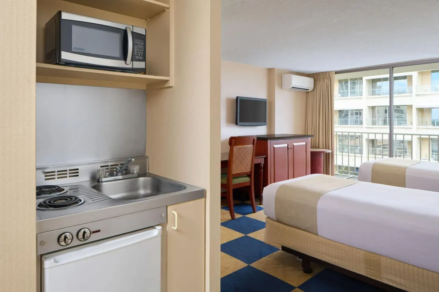 Guest room kitchenette with sink, stovetop, microwave, and bed at Ewa Hotel Waikiki.